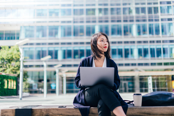 Woman with laptop sitting on bench in city