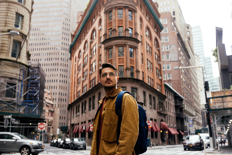 Portrait of a young man wearing a brown jacket, backpack and glasses on the street in New York City, USA