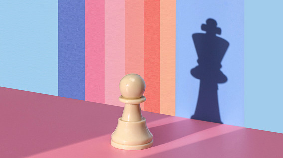 A white chess pawn stands on a pink surface, casting a shadow of a king on a pastel-colored striped background. The vibrant hues transition from blue to pink, creating a gradient effect. The image symbolizes potential, transformation, and ambition.