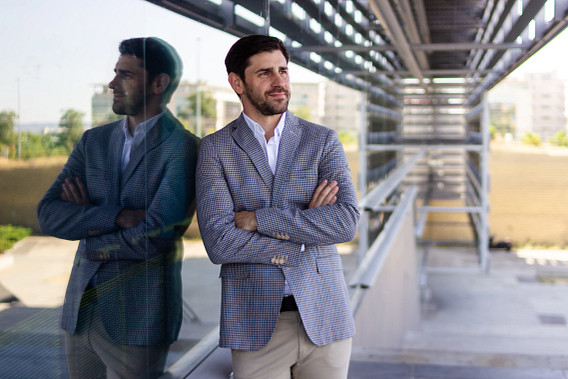 Businessman weating grey blazer, leaning on the glass exterior of a modern office building with arms crossed